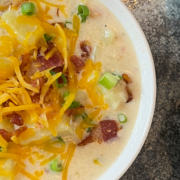 potato soup in a bowl topped with bacon, chives, and cheddar cheese